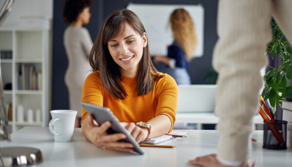 Young woman is talking to his colleague in the office, two women discuss behind her in front of whiteboard