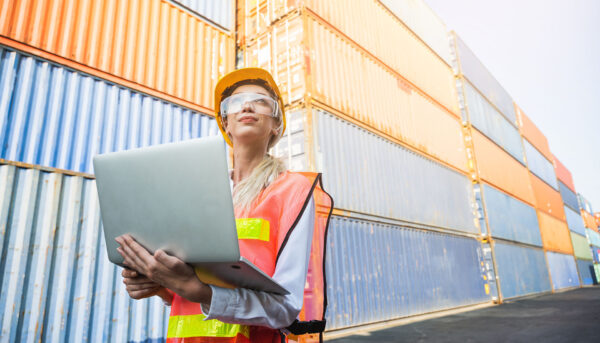 female foreman worker holding clipboard, in front of shipping containers