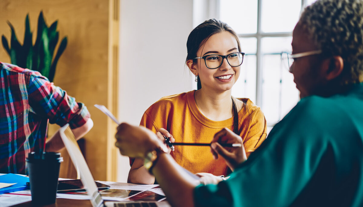 young woman sitting at table and talking to female colleague