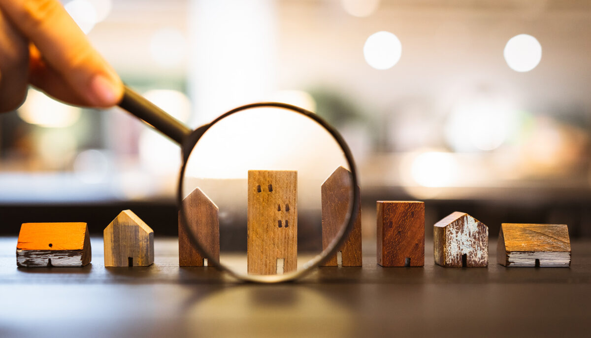 Hand holding magnifying glass and looking at house model